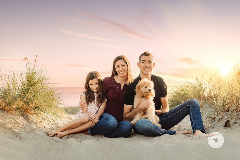 parents sit with daughter and new puppy during sunset Rexhame Beach family photos