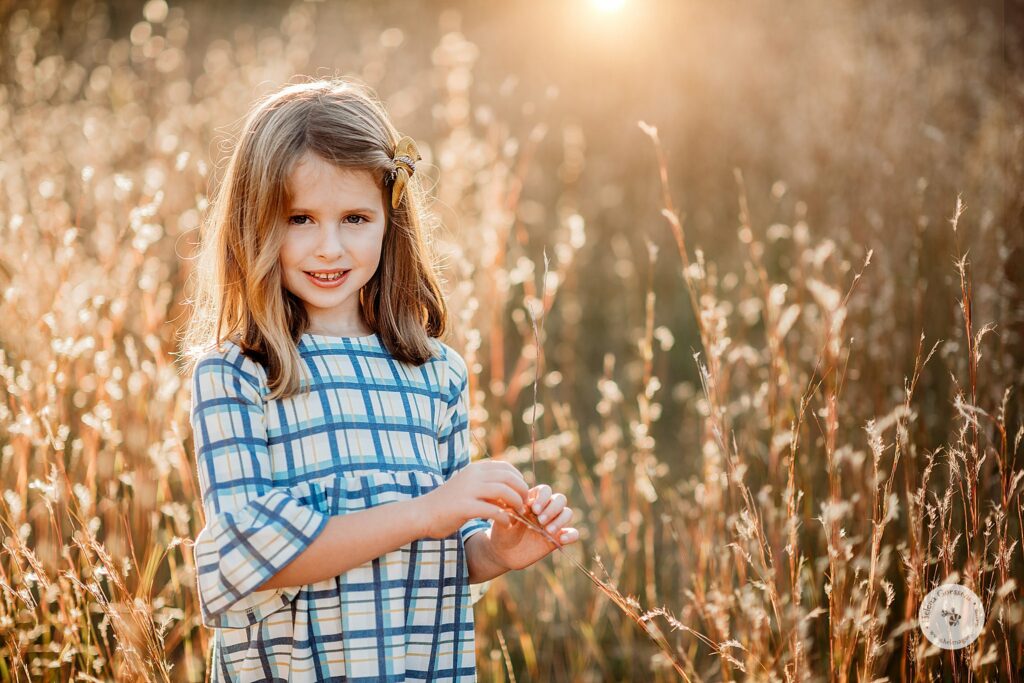 girl in blue and yellow plaid dress plays with grass in field in Concord MA