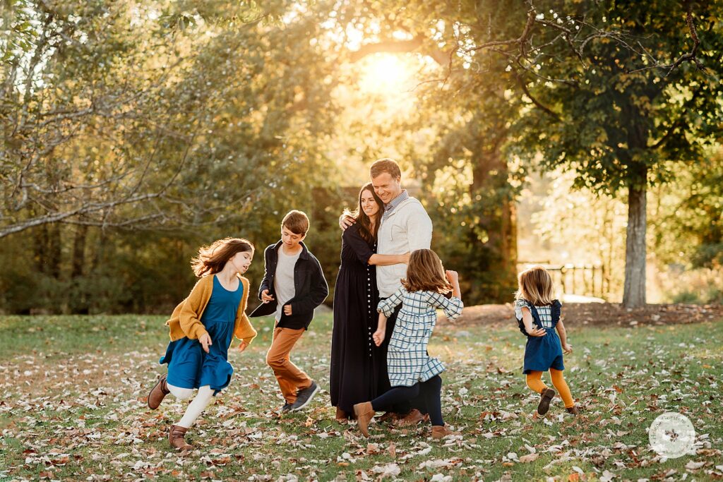 parents hug while four kids run around them during family portraits at the Old Manse