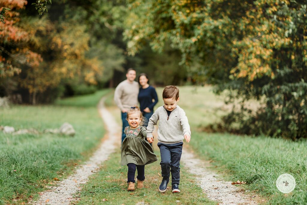 brother and sister walk up path while mom and dad hug behind them during fall family photos 