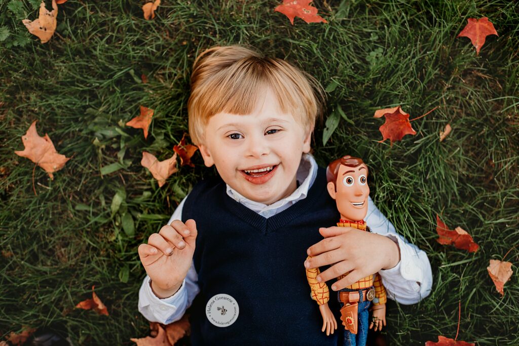 toddler holds Cowboy Woody from Toy Story laying in leaves at Larz Anderson Park 