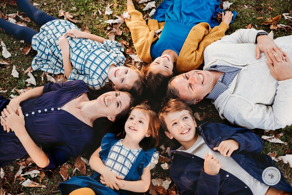 family of six lays in grass and leaves during family portraits at the Old Manse