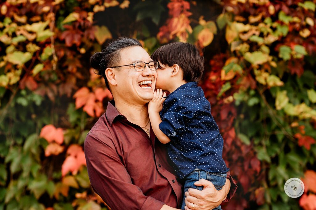 son whispers to dad during fall family photos in Brookline MA 