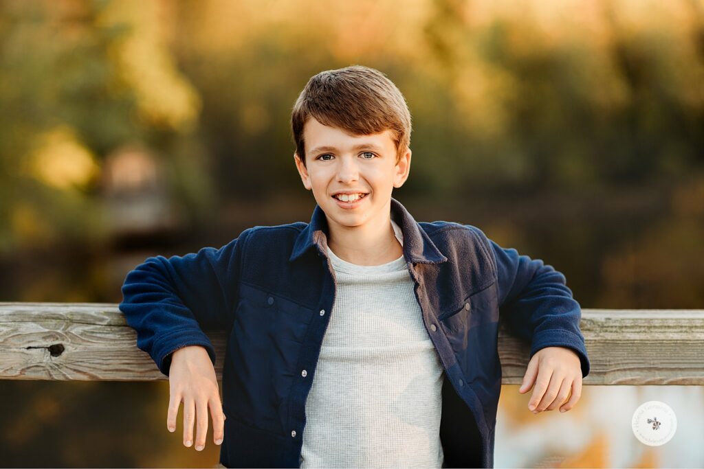 boy in blue shirt leans against wooden bridge during family photos