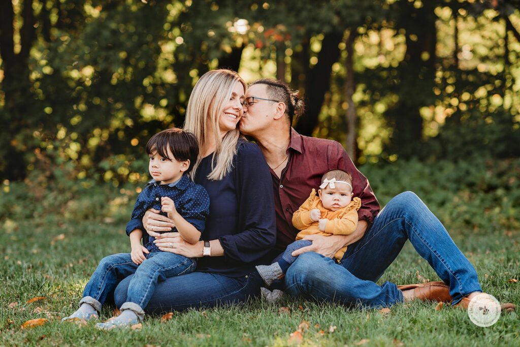 husband kisses wife's cheek during fall Larz Anderson Park family photos