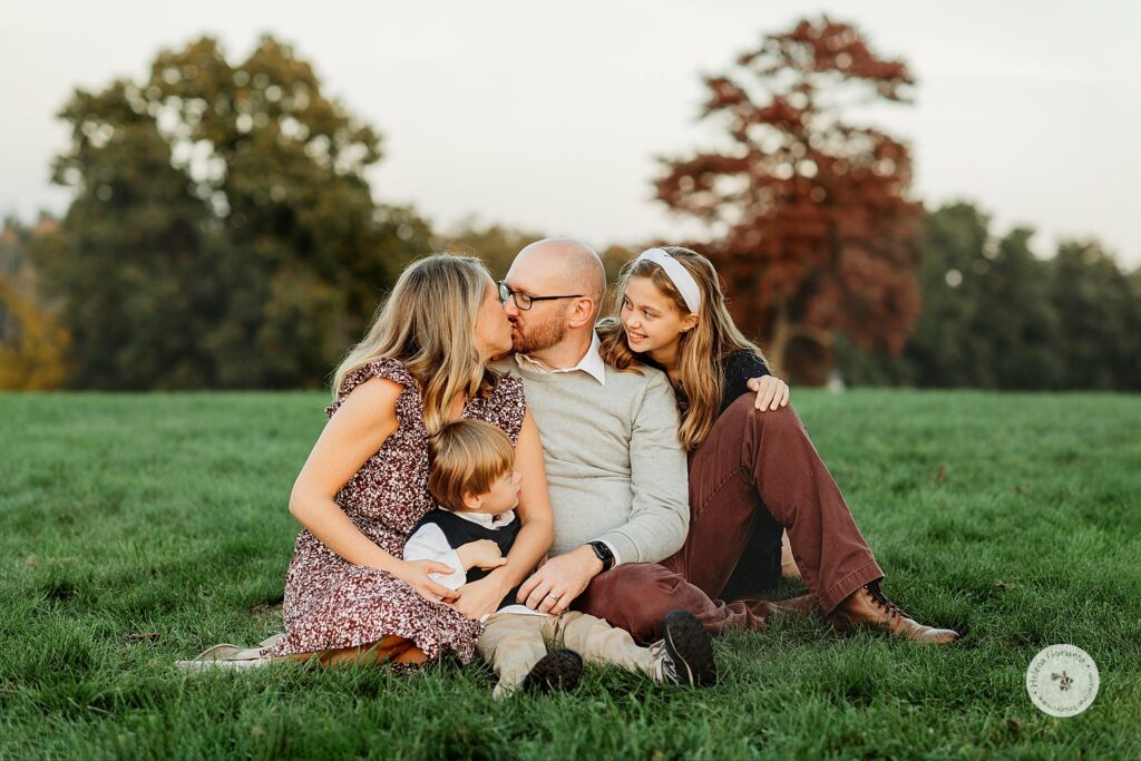 parents kiss while holding onto kids during fall family portraits at Larz Anderson Park
