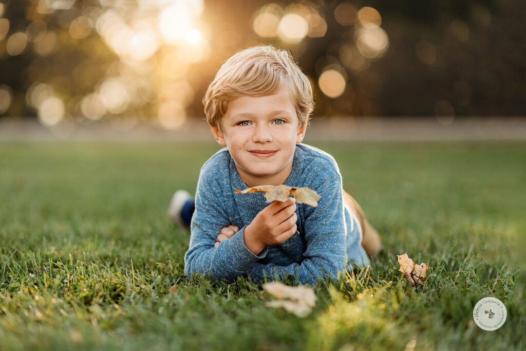 boy lays in grass playing with leaves during Sunset Family Portraits at Larz Anderson Park