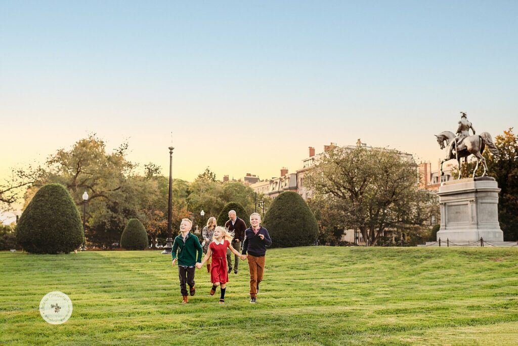 family of five walks through Public Garden at sunset by monument 