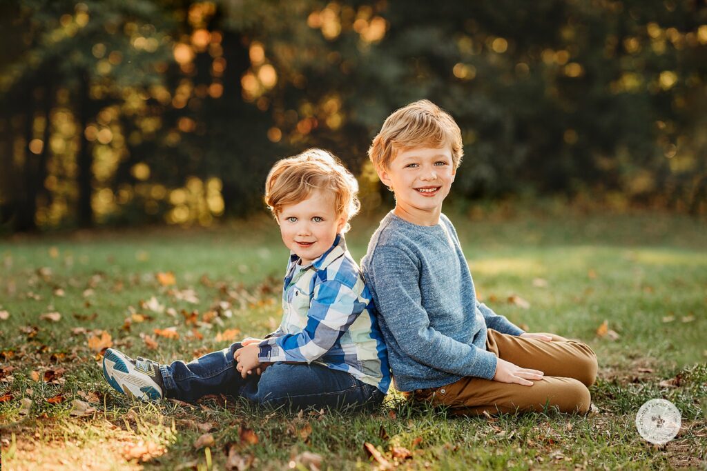 boys sit back to back during Sunset Family Portraits at Larz Anderson Park