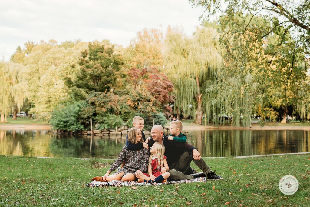 parents sit on blanket by pond at Boston Public Garden with kids around them 