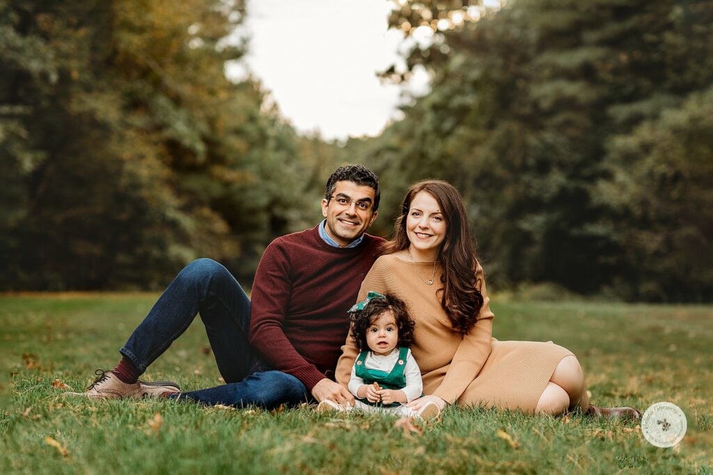 family of three sits together in grass during Fall Bradley Estate Family Portraits