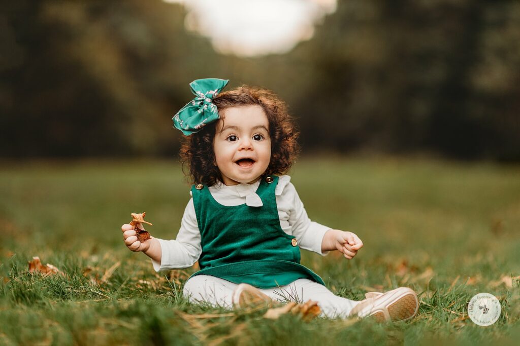toddler girl in green jumper plays in leaves during Fall Bradley Estate Family Portraits