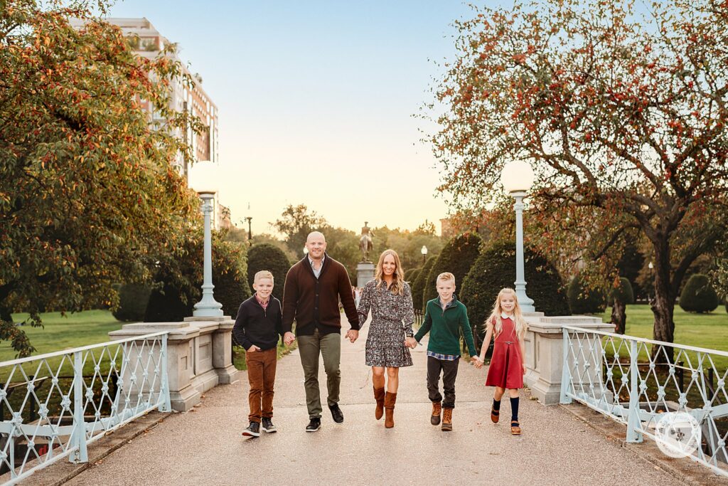 family of five holds hands walking over bridge during Public Garden Family Portraits