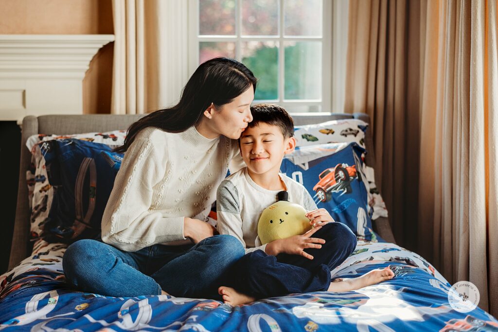 mom sits with son on bed during lifestyle family photos in Weston MA