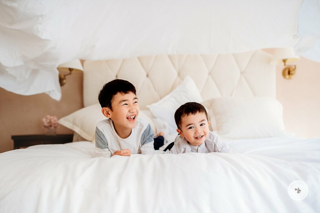 brothers lay on bed while family tosses sheets above them 