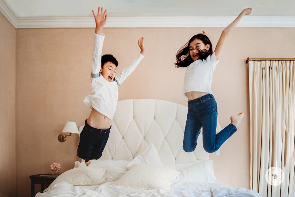 kids jump on bed during lifestyle family photos in Weston MA