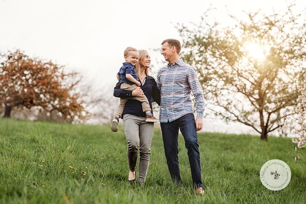 couple walks down hill holding toddler son during family photos in MA