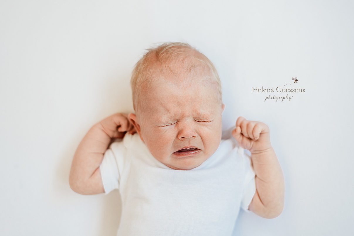 baby girl cries during newborn photos at home on white sheet 