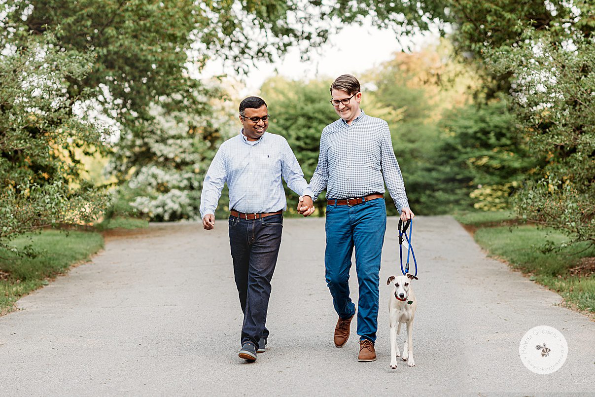 married couple holds hands walking dog down path at Peter's Hill during family photos 