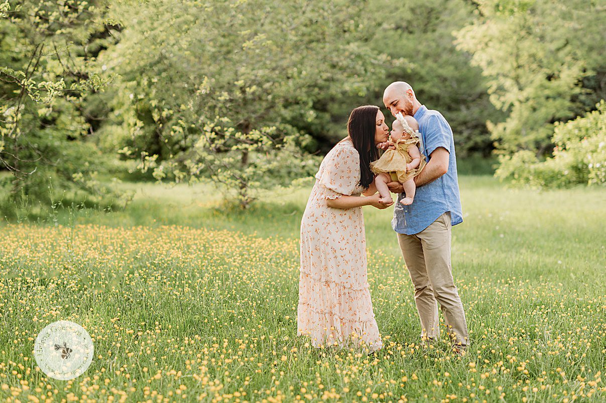 dad holds daughter while mom leans to kiss her during Spring Family Portraits at Peter's Hill