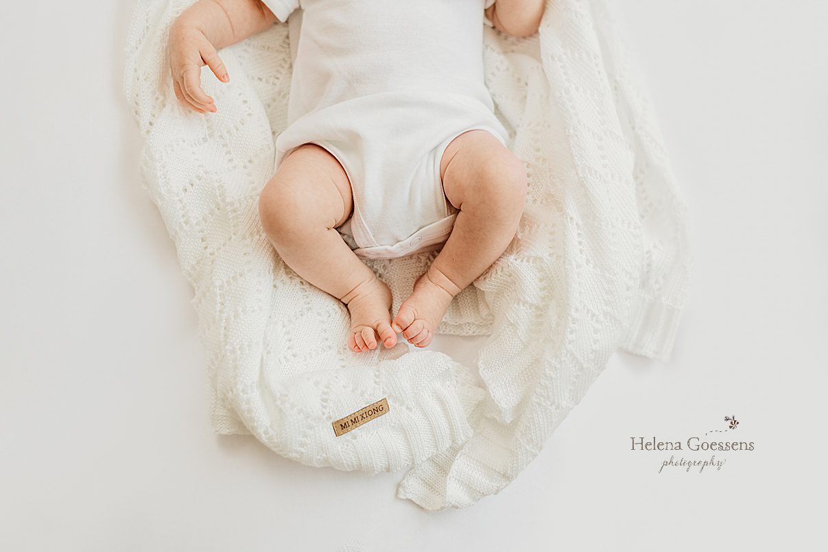 baby girl in white onesie lays on knit white scarf during newborn photos