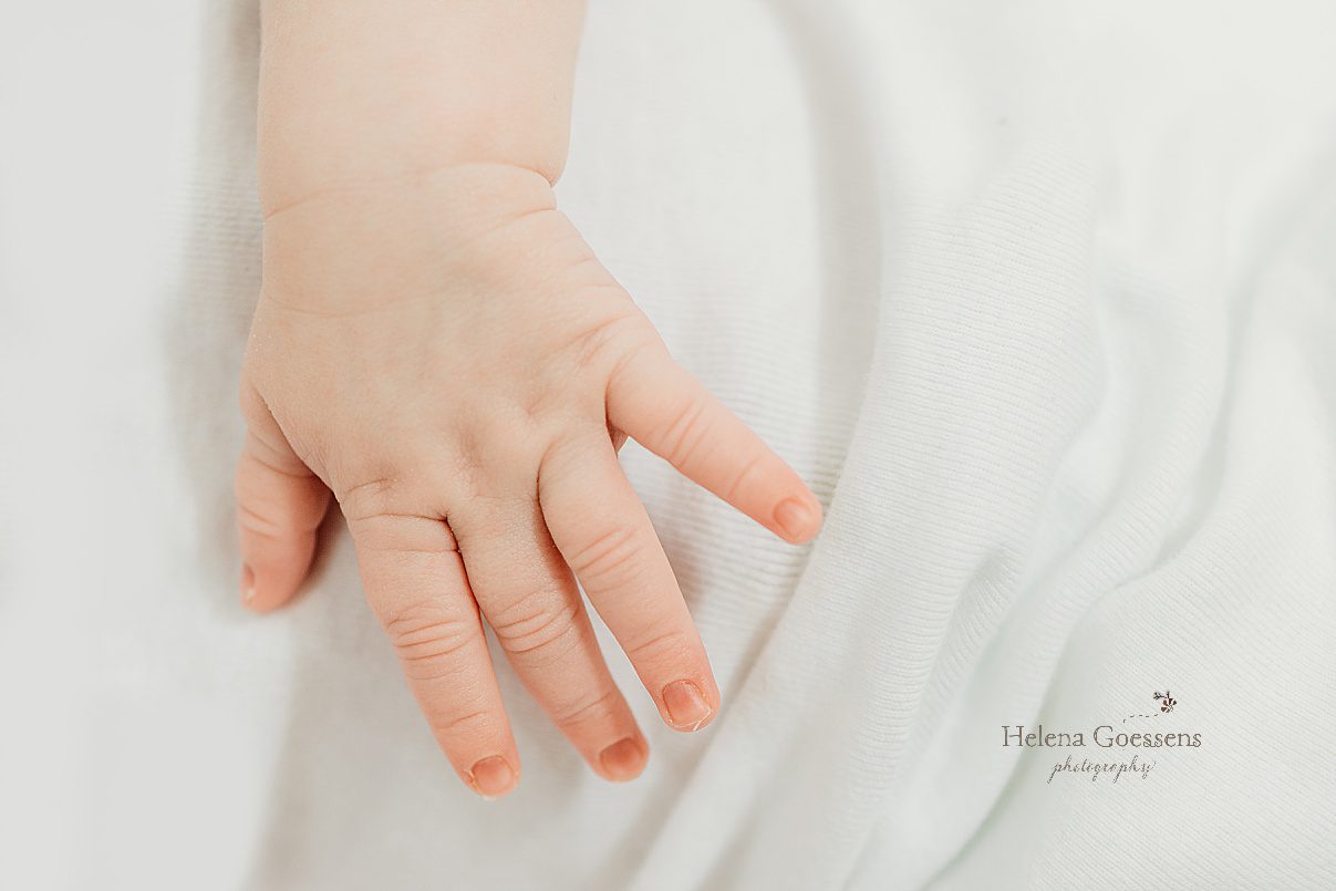 baby's hand lays on white blanket during lifestyle newborn portraits in Dedham MA