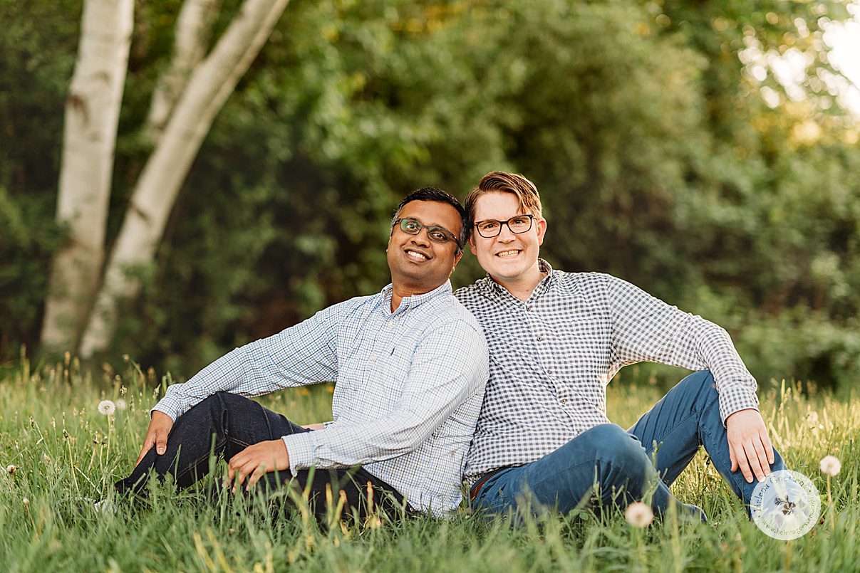 couple sits together in tall grass leaning together during Jamaica Plain family portraits