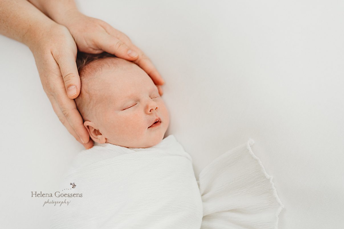 parent holds baby's head in simple white wrap during newborn photos at home