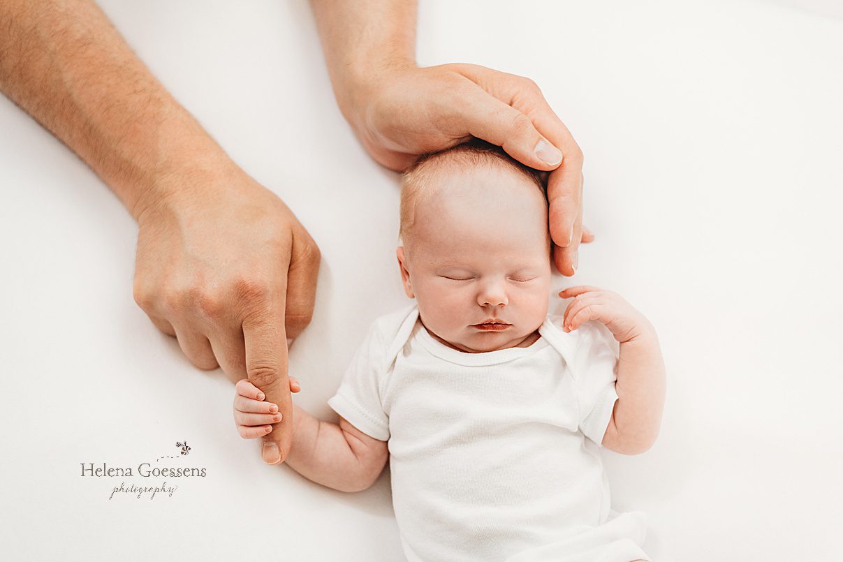 dad holds baby girl's head and finger during newborn photos at home