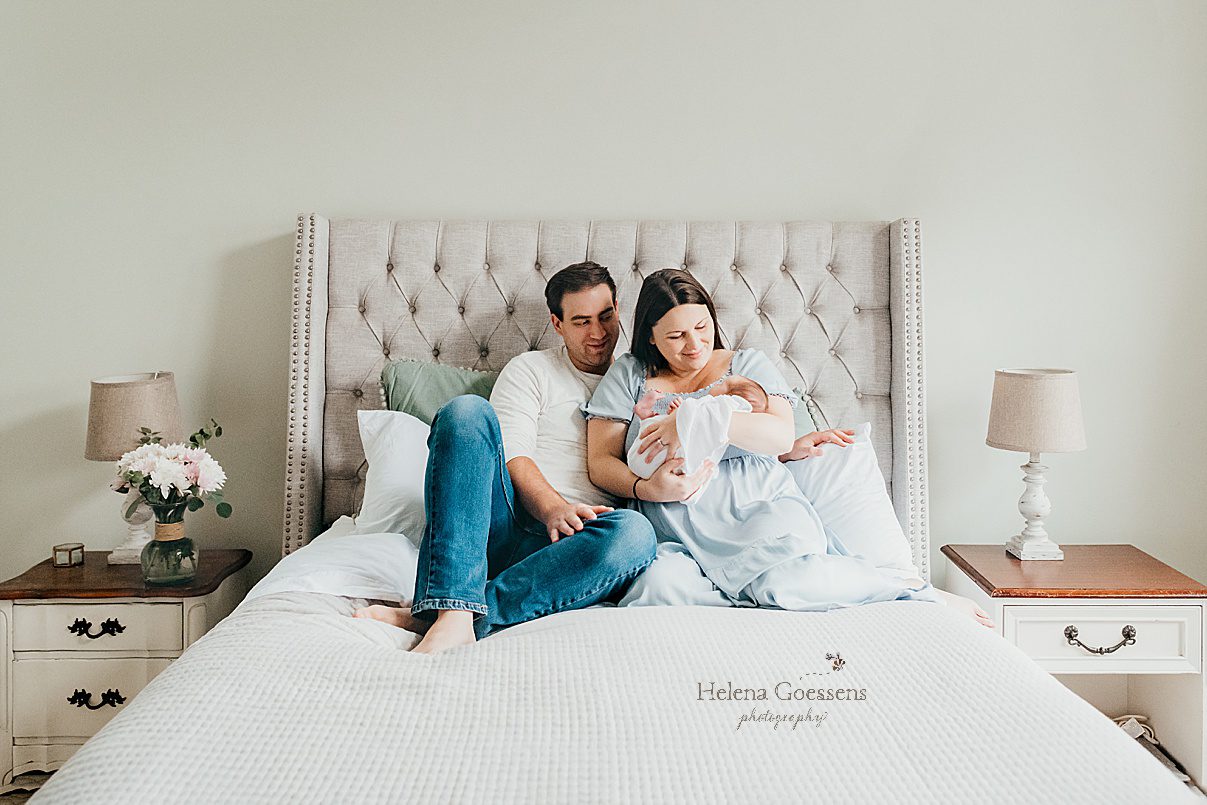 new parents sit on bed with baby girl during Randolph MA newborn session