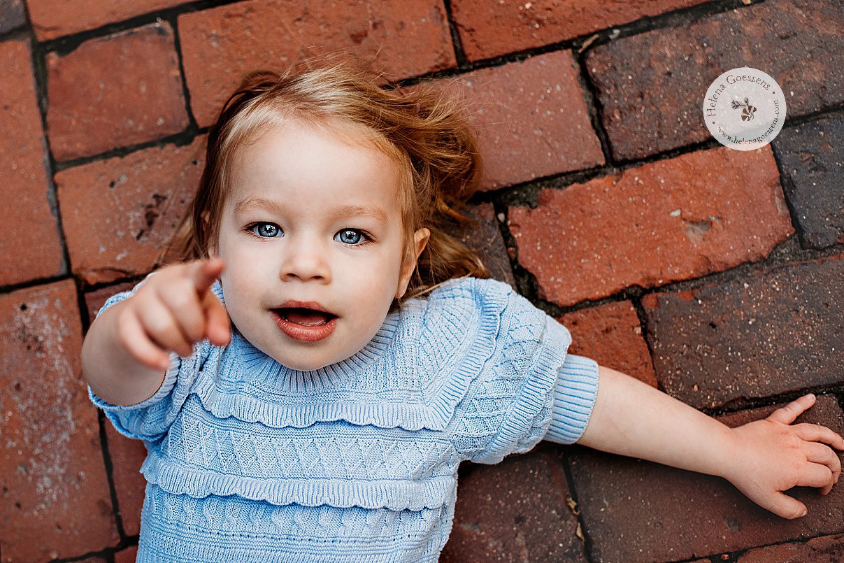 toddler in blue sweater lays on bricks in Boston MA during family photos 