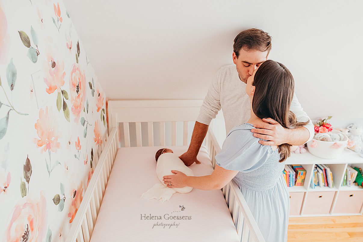 parents kiss with little girl in crib photographed by Boston MA newborn photographer Helena Goessens Photography 