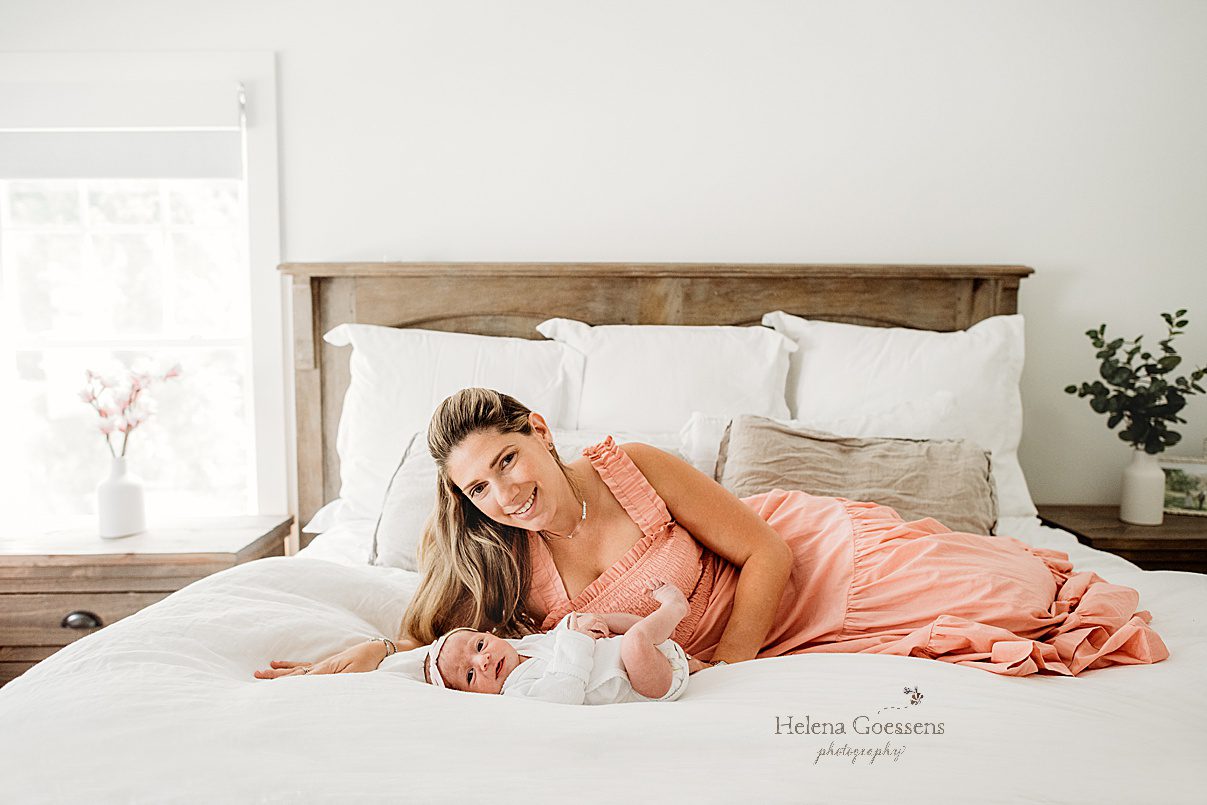 mother lays on bed with newborn in pink dress during lifestyle newborn session 
