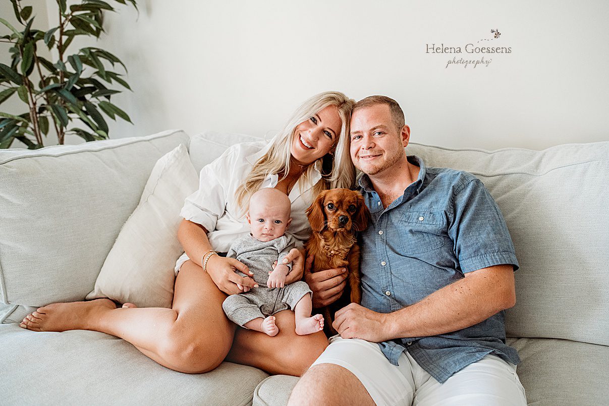 parents sit on couch with baby and dog during newborn session in Foxborough apartment