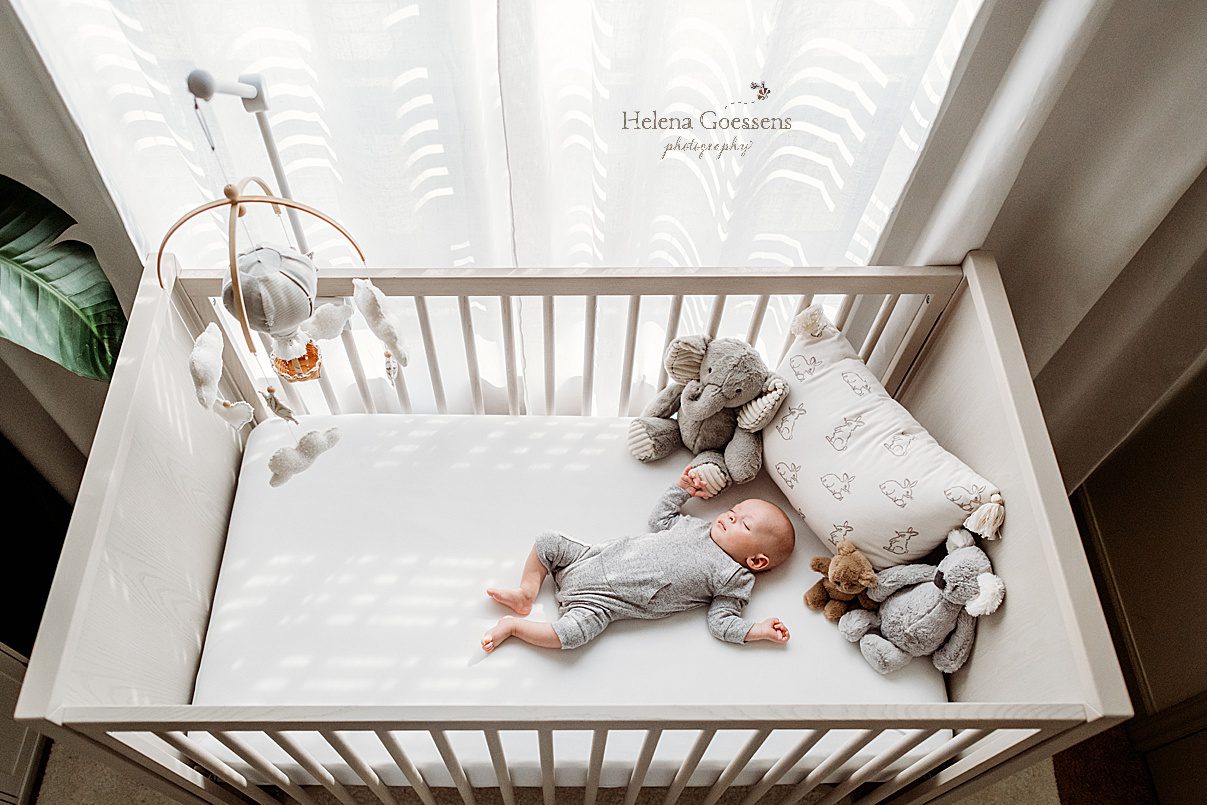 baby lays in crib on back in grey sleeper photographed by MA newborn photographer Helena Goessens Photography 