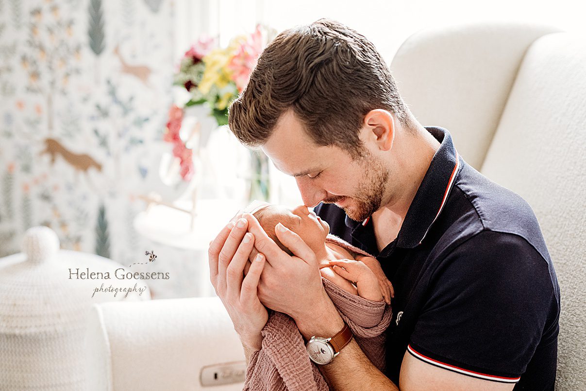 dad snuggles with baby girl in white chair in nursery during Dedham MA lifestyle newborn portraits 