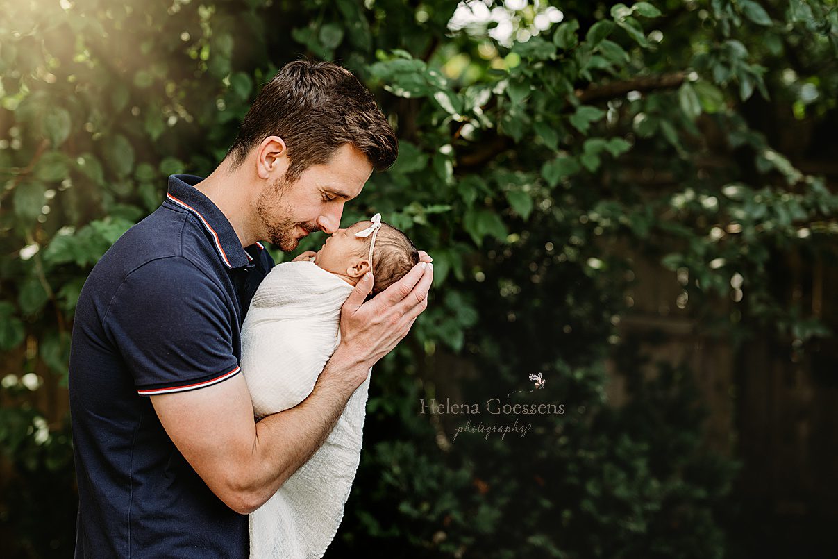 dad nuzzles baby girl's nose standing with her outside in wrap 