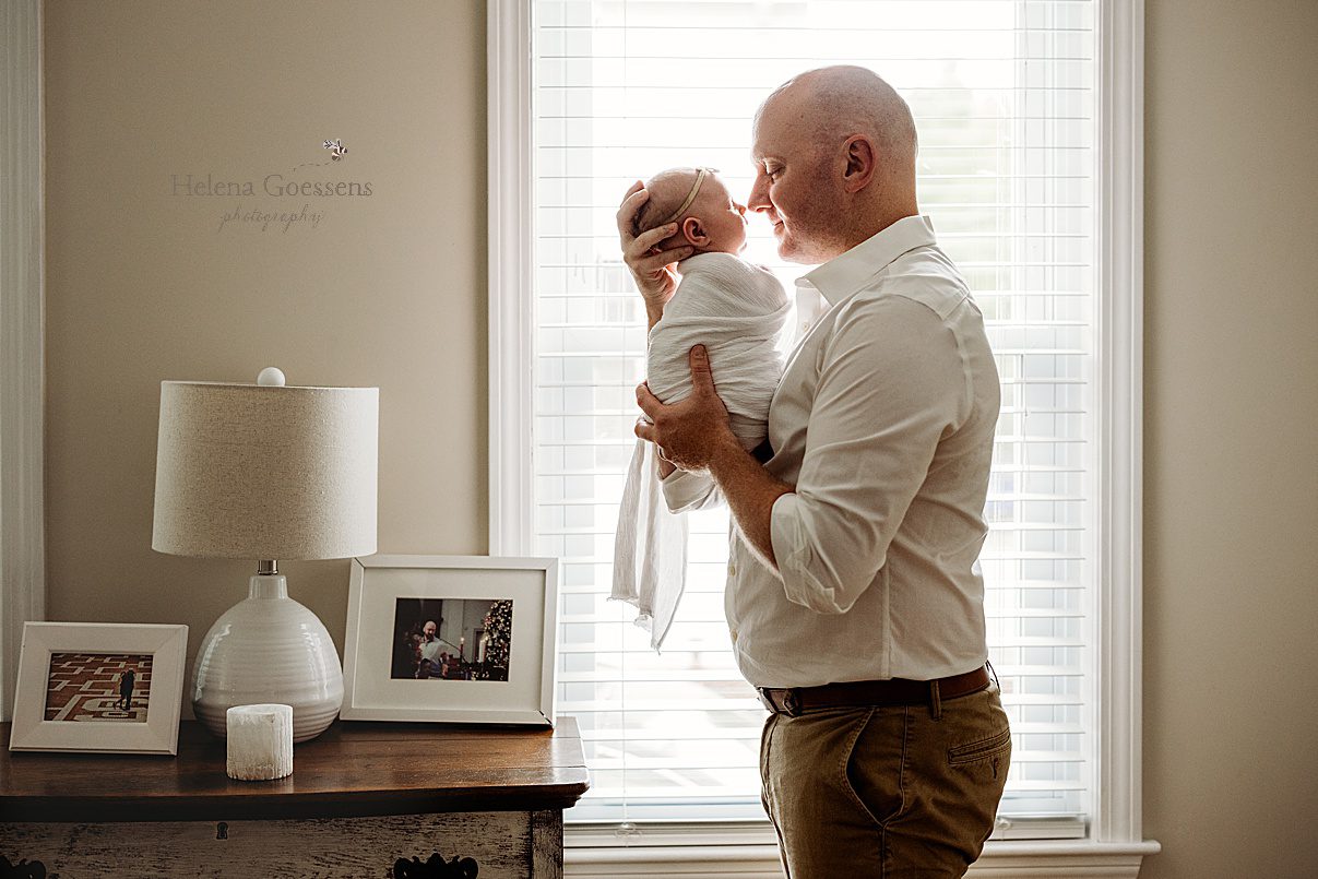 dad brings baby girl up to nuzzle noses with her during lifestyle newborn session in Newton MA