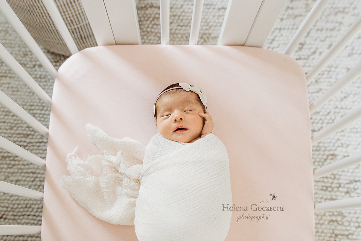 baby girl lays in white wrap with hand on cheek during Dedham MA lifestyle newborn portraits in nursery 