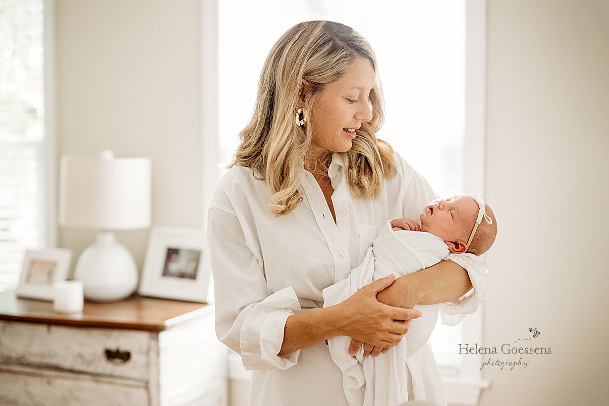mom smiles down at baby girl sleeping in her arms during lifestyle newborn session in Newton MA