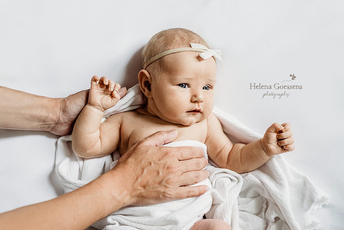 baby girl lays on back in white knit blanket during lifestyle newborn session in Newton