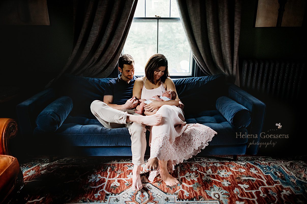 parents sit on navy blue couch with newborn baby girl during lifestyle newborn photos at home