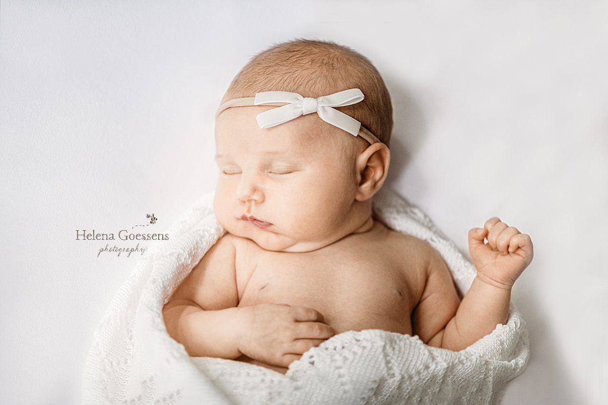 baby girl lays on back in white crocheted blanket with simple white bow on head during Newton MA lifestyle newborn session