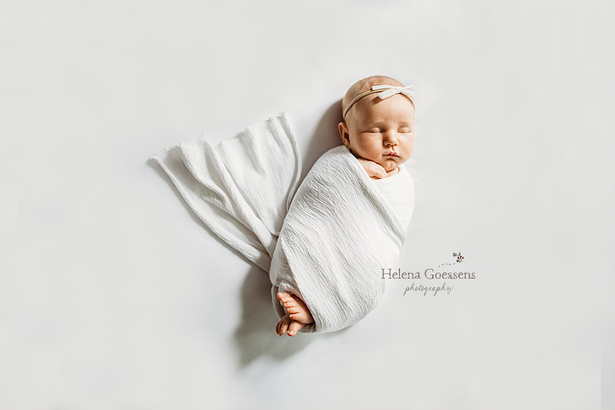 baby girl sleeps in white linen wrap with white bow on head during photos at home 