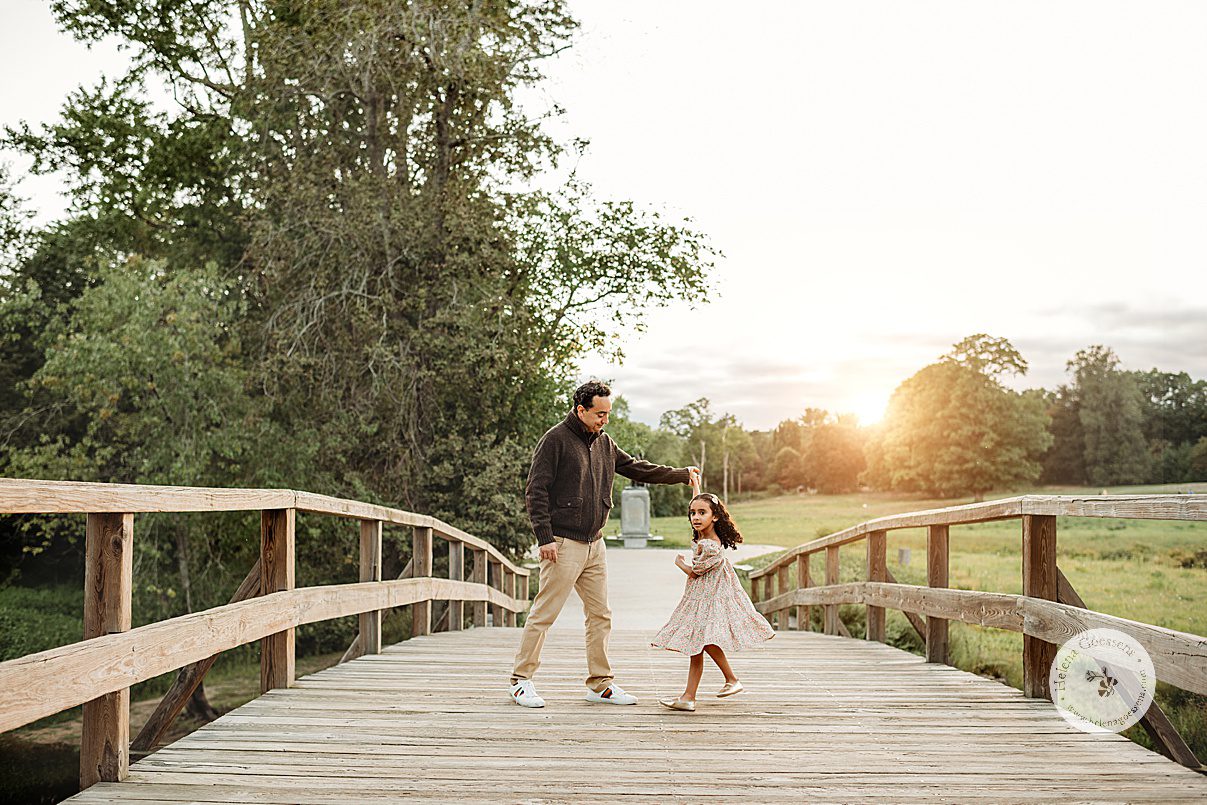 dad twirls daughter on wooden bridge during Concord MA family portrait session in the fall