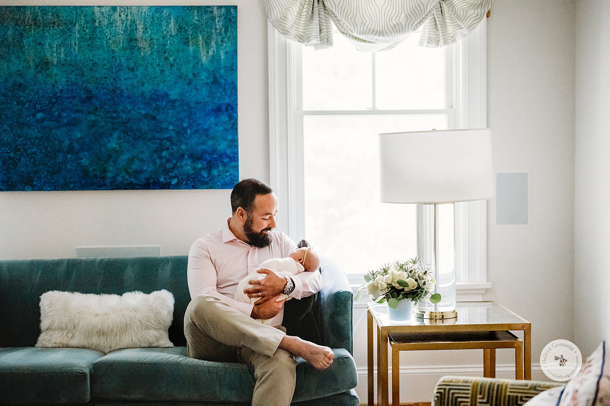 dad sits on couch holding newborn daughter in arms during lifestyle photos at home 