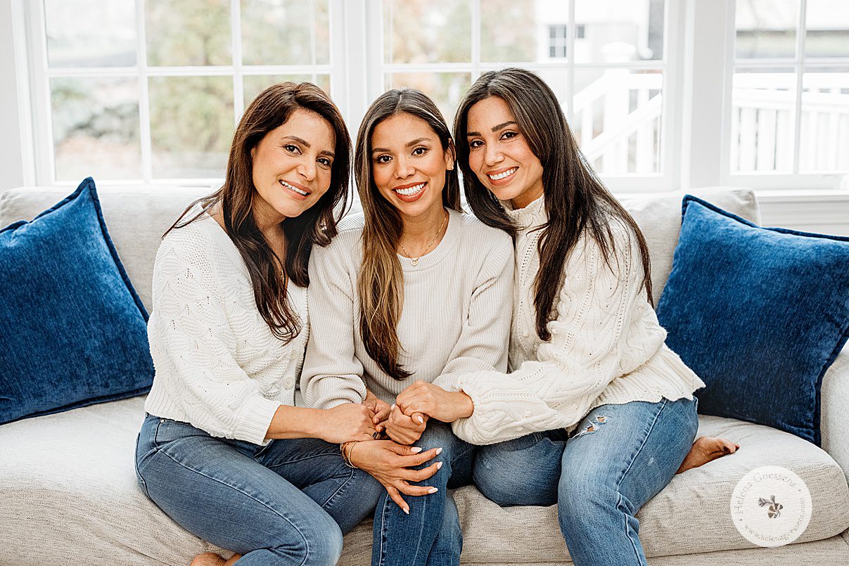 three sisters sit on tan couch hugging during generational family portraits in Boston MA