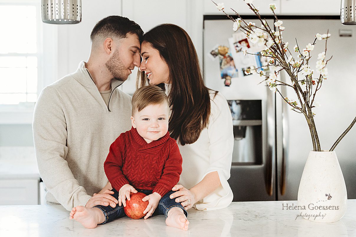 parents lean heads together with son sitting on counter between them during lifestyle family photos at home in Boston MA