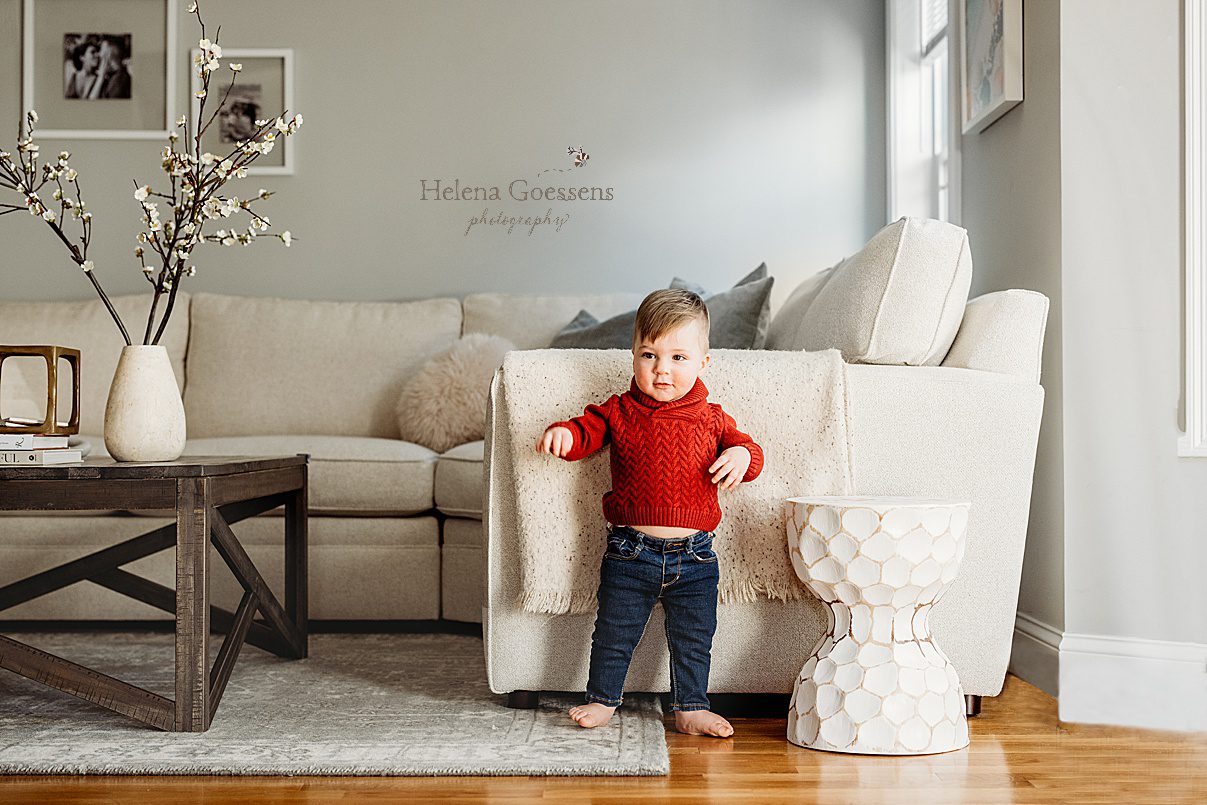 one year old walks through apartment in red sweater and jeans during family photos in Boston MA