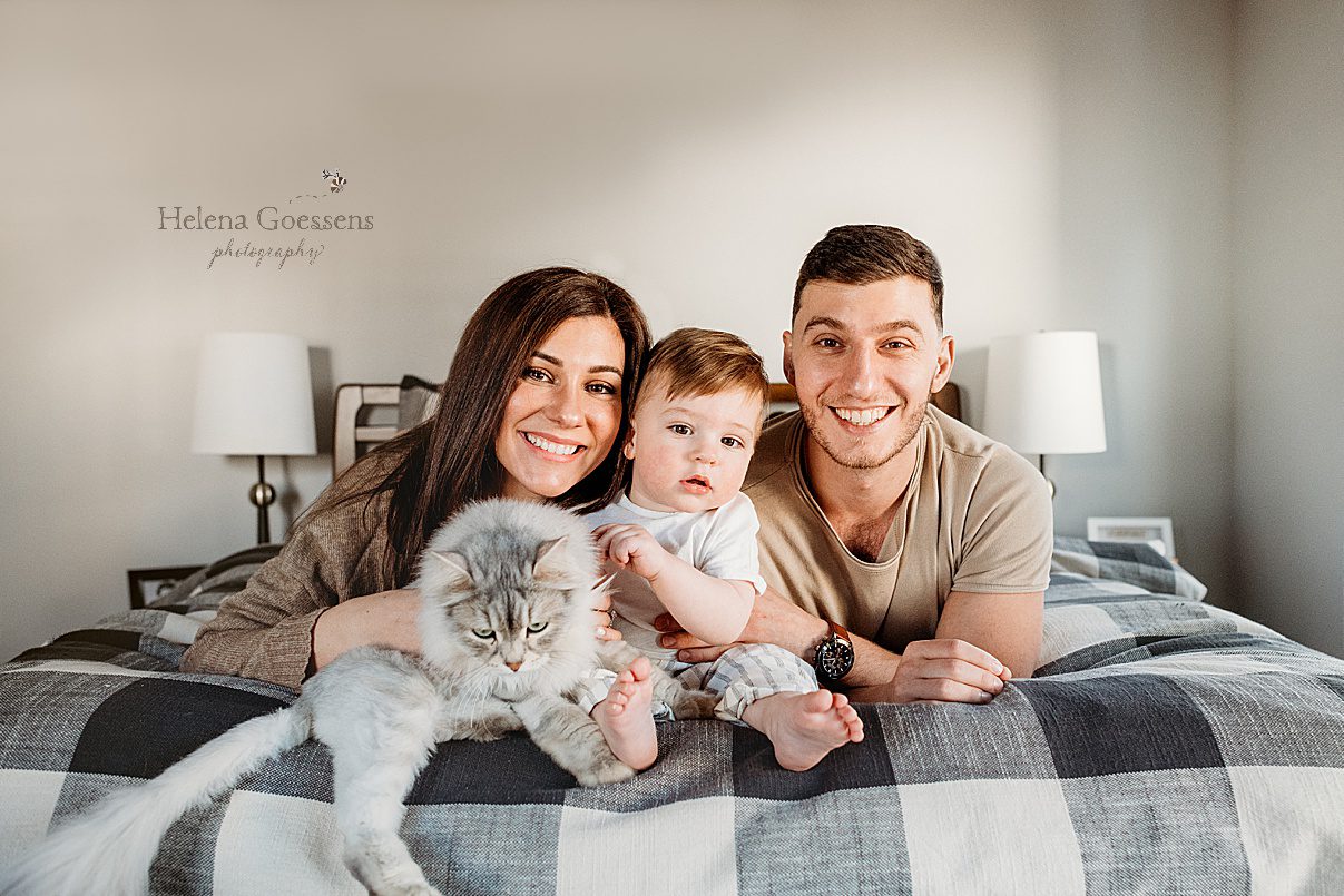 family of three lays on bed with grey cat during family photos at home in Boston MA home